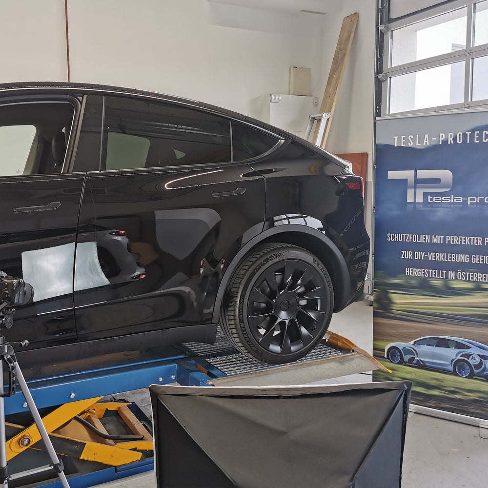 Schwarzes Tesla Model Y auf der Hebebühne vor einem Tesla-Protect Banner